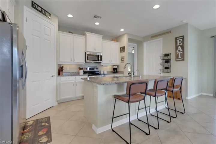 Kitchen featuring appliances with stainless steel finishes, a sink, light tile patterned flooring, light stone counters, and a breakfast bar area