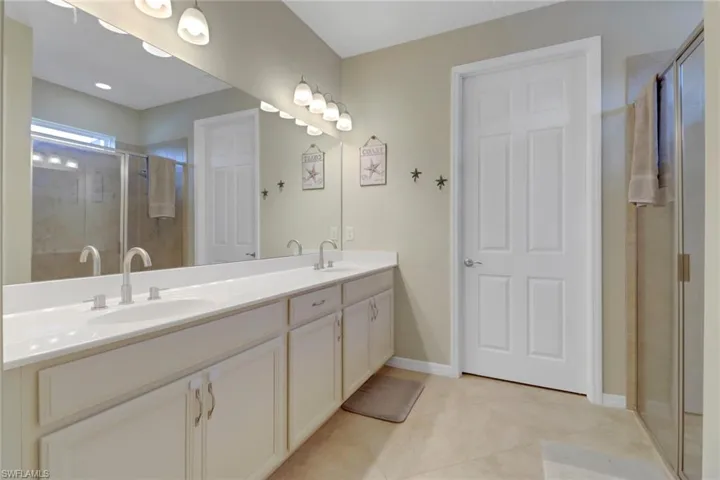 Full bath featuring a shower stall, double vanity, tile patterned flooring, and baseboards