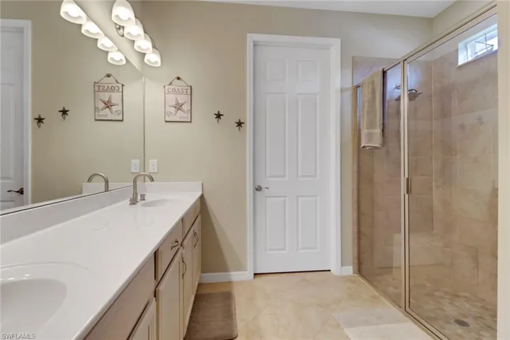Full bath with a shower stall, double vanity, tile patterned flooring, and baseboards