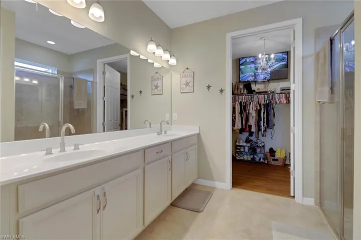 Full bathroom with a stall shower, a walk in closet, double vanity, tile patterned flooring, and baseboards