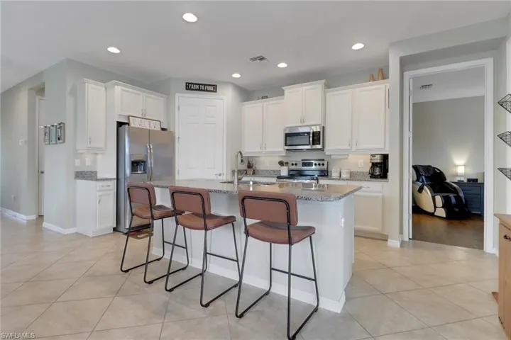 Kitchen featuring appliances with stainless steel finishes, a sink, white cabinetry, light tile patterned floors, and a breakfast bar area