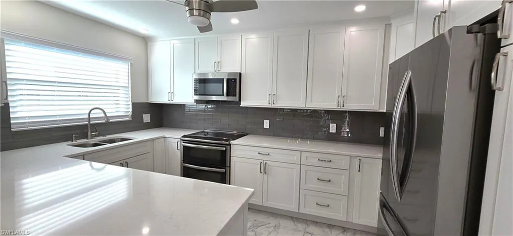 Kitchen featuring stainless steel appliances, white cabinets, decorative backsplash, light stone countertops, and recessed lighting