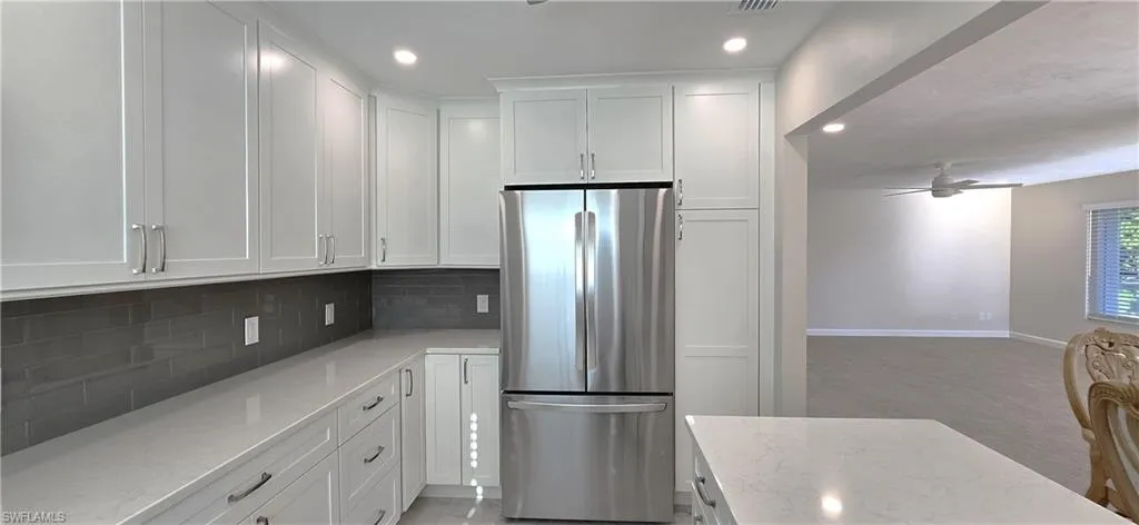 Kitchen featuring freestanding refrigerator, white cabinets, recessed lighting, light stone countertops, and a ceiling fan