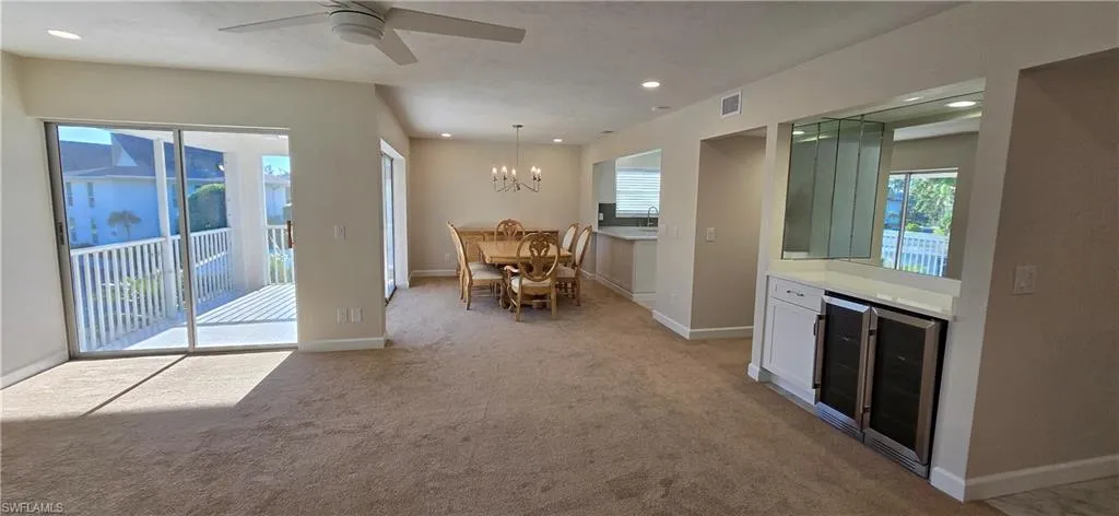 Dining room with light colored carpet, beverage cooler, recessed lighting, a ceiling fan, and a chandelier