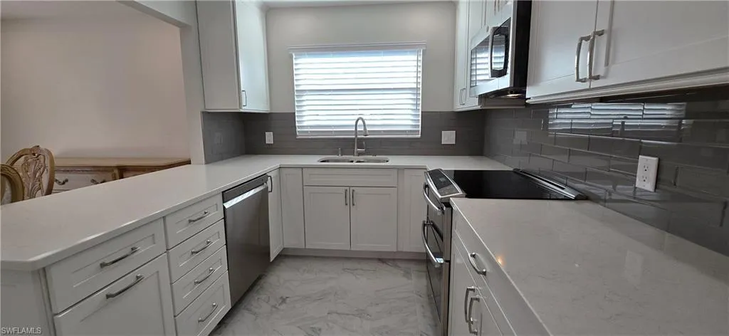 Kitchen featuring stainless steel appliances, tasteful backsplash, light marble finish floors, white cabinets, and light stone counters