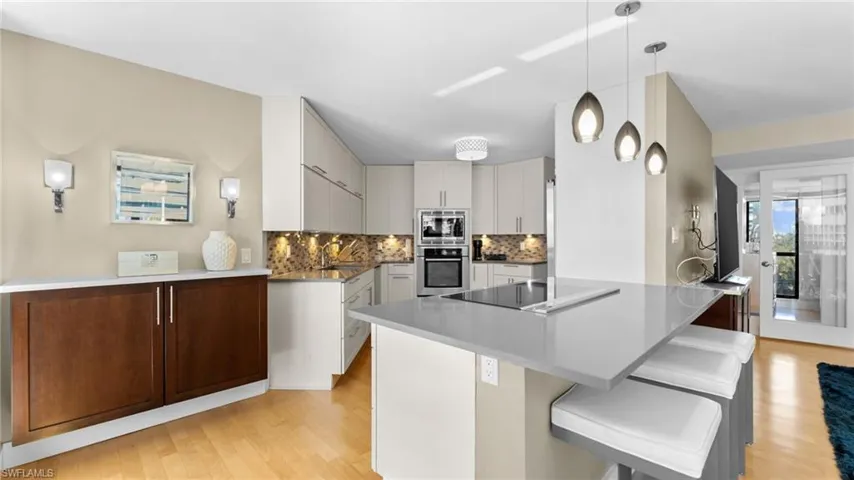 Kitchen with tasteful backsplash, black electric stovetop, pendant lighting, light hardwood / wood-style floors, and stainless steel microwave