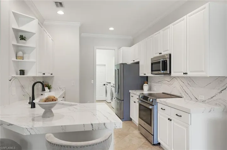 Kitchen with light tile patterned floors, kitchen peninsula, backsplash, washer and dryer, and stainless steel appliances