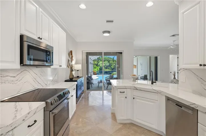 Kitchen with light tile patterned flooring, white cabinetry, crown molding, light stone countertops, and appliances with stainless steel finishes