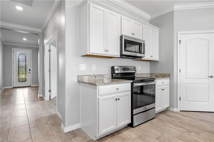 Kitchen with white cabinetry, appliances with stainless steel finishes, baseboards, and ornamental molding