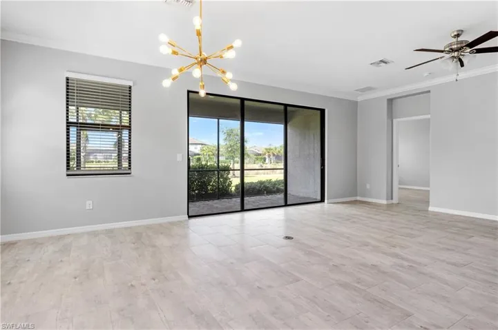 Spare room with baseboards, ornamental molding, visible vents, and ceiling fan with notable chandelier
