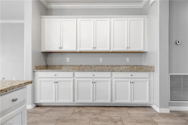 Kitchen featuring white cabinets, light stone countertops, baseboards, and ornamental molding