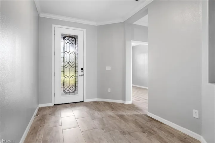 Entryway with light wood-style flooring, crown molding, and baseboards