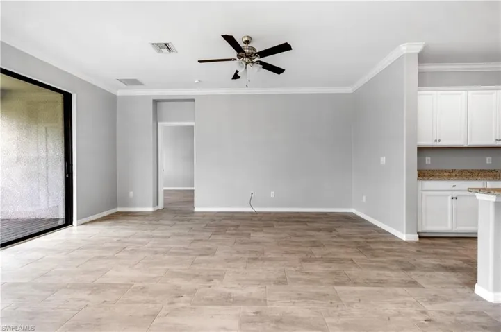 Unfurnished living room featuring crown molding, visible vents, a ceiling fan, and baseboards