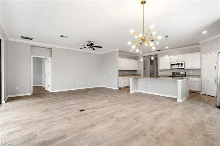 Kitchen with stainless steel appliances, a center island with sink, open floor plan, visible vents, and ornamental molding