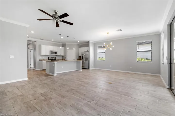 Unfurnished living room featuring recessed lighting, crown molding, baseboards, and ceiling fan with notable chandelier