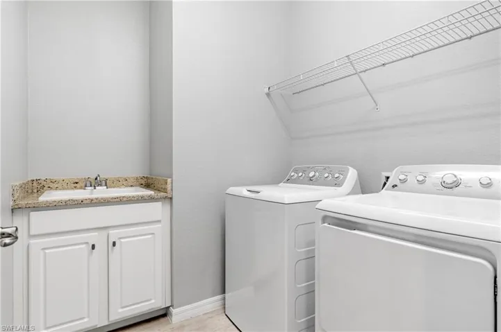 Washroom featuring washing machine and dryer, baseboards, and a sink