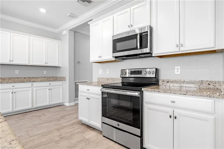 Kitchen with light wood finished floors, stainless steel appliances, visible vents, white cabinetry, and ornamental molding