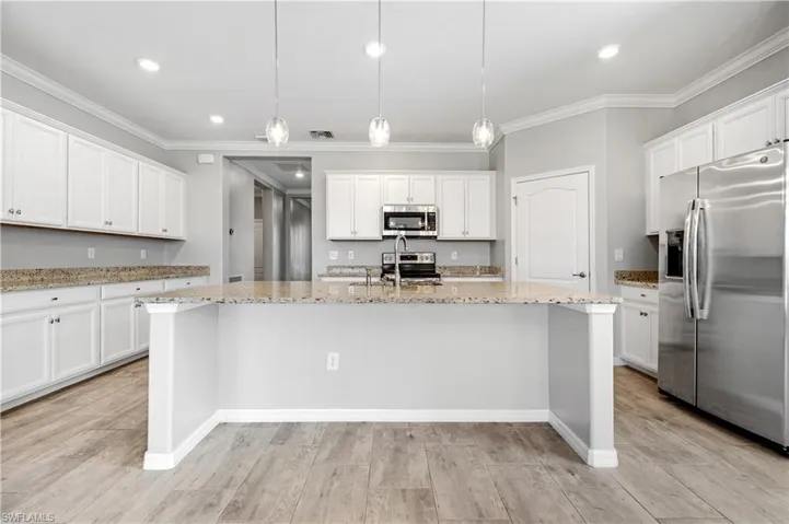 Kitchen featuring light stone countertops, crown molding, a center island with sink, appliances with stainless steel finishes, and white cabinetry