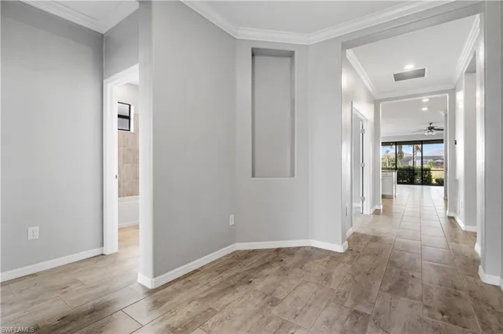 Hallway with baseboards, ornamental molding, wood finished floors, and visible vents