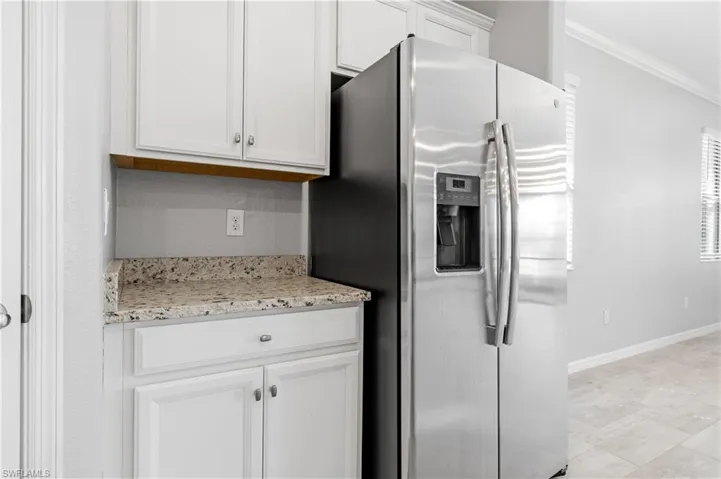 Kitchen featuring light stone counters, crown molding, baseboards, stainless steel refrigerator with ice dispenser, and white cabinetry