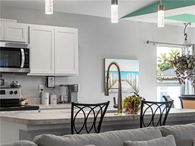 Kitchen with appliances with stainless steel finishes, light countertops, white cabinets, a kitchen breakfast bar, and pendant lighting
