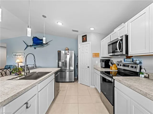 Kitchen featuring appliances with stainless steel finishes, white cabinets, light countertops, hanging light fixtures, and vaulted ceiling
