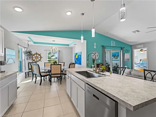 Kitchen with white cabinetry, stainless steel dishwasher, decorative light fixtures, light countertops, and vaulted ceiling