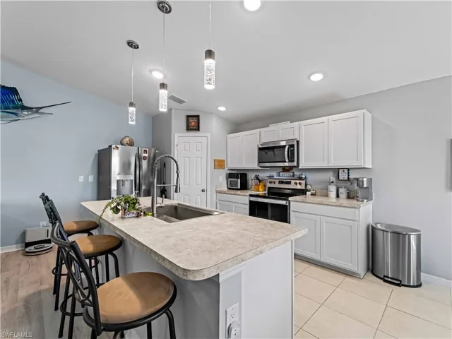 Kitchen with light countertops, a breakfast bar, stainless steel appliances, an island with sink, and white cabinetry