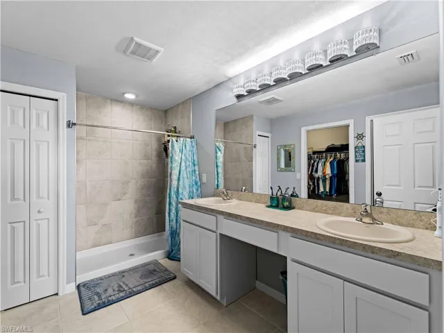 Bathroom with a spacious closet, double vanity, a shower stall, and light tile patterned flooring