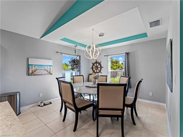 Dining area with a tray ceiling, a chandelier, and light tile patterned flooring
