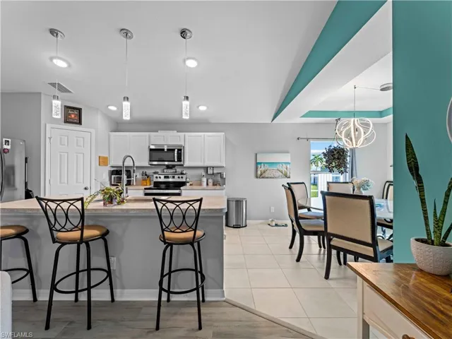 Kitchen with hanging light fixtures, white cabinetry, stainless steel appliances, a kitchen bar, and butcher block counters