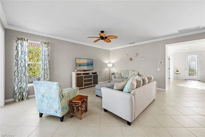 Living room featuring ornamental molding, light tile patterned floors, and ceiling fan