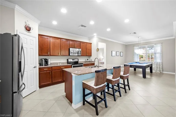 Kitchen featuring ornamental molding, stainless steel appliances, billiards table, a breakfast bar, and light stone counters