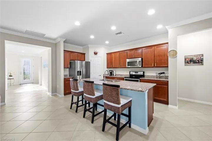 Kitchen with a breakfast bar, crown molding, an island with sink, appliances with stainless steel finishes, and recessed lighting