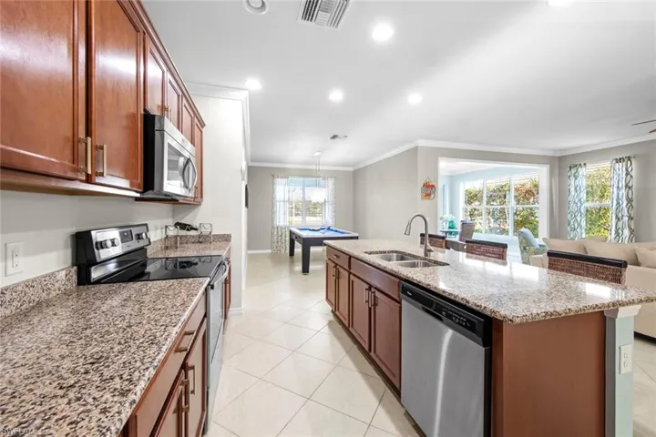 Kitchen with appliances with stainless steel finishes, recessed lighting, crown molding, light stone countertops, and open floor plan