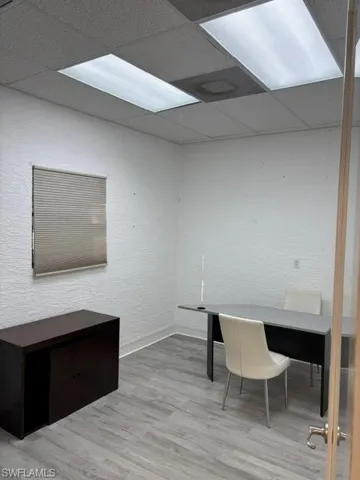 Unfurnished office featuring light wood finished floors, a textured wall, and a paneled ceiling