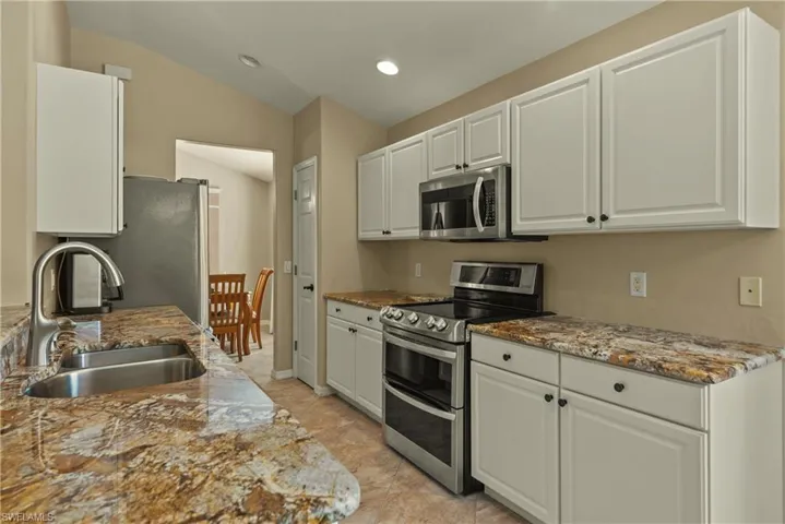 Kitchen with stainless steel appliances, dark stone counters, white cabinets, recessed lighting, and lofted ceiling