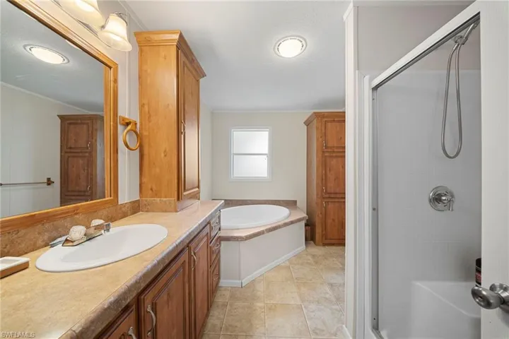 Bathroom featuring a built-in jetted tub, a separate shower enclosure with a glass door, a single vanity with an integrated sink, and ample storage provided by wood-finish cabinetry