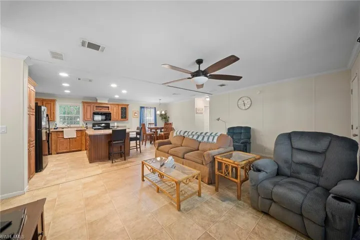 Open concept living area with tile flooring throughout, featuring a kitchen with wood cabinetry and black appliances, a dining area, and a living room with a ceiling fan