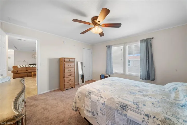 Carpeted bedroom featuring a ceiling fan with light fixture, white trim, and two windows with blinds