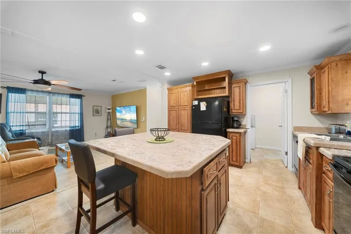Kitchen featuring a central island with countertop seating, wood-finish cabinetry, black appliances, and tile flooring
