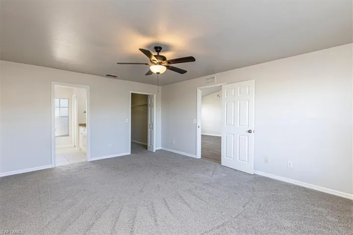 Unfurnished bedroom featuring a walk in closet, light colored carpet, ceiling fan, and ensuite bath