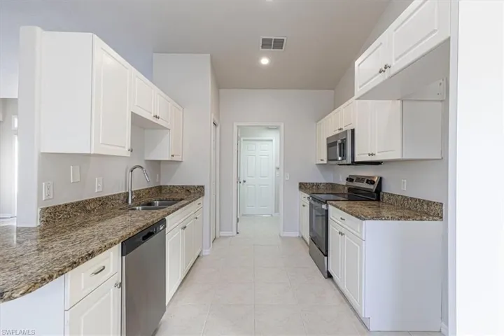 Kitchen with appliances with stainless steel finishes, dark stone counters, white cabinets, and recessed lighting