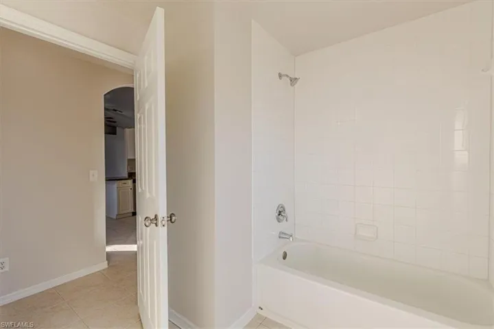 Full bath with washtub / shower combination and light tile patterned floors