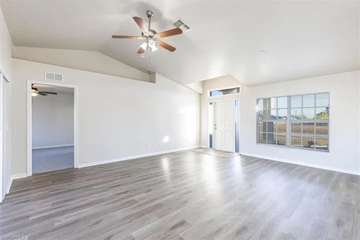 Unfurnished living room featuring ceiling fan, vaulted ceiling, and light wood-style flooring
