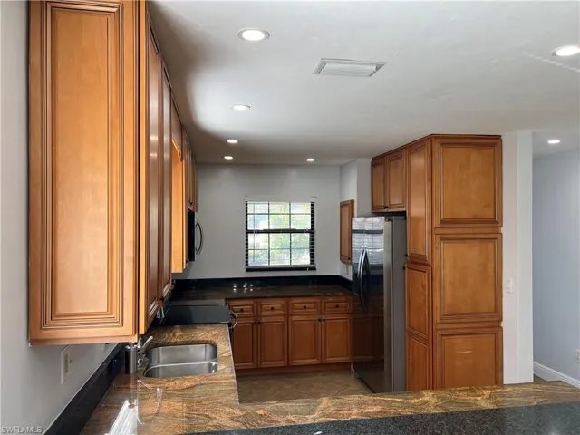 Kitchen featuring wood finish cabinets, freestanding refrigerator, dark stone countertops, recessed lighting, and tile patterned flooring