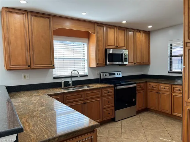 Kitchen with stainless steel appliances, wood finish cabinets, recessed lighting, dark stone counters, and light tile patterned floors
