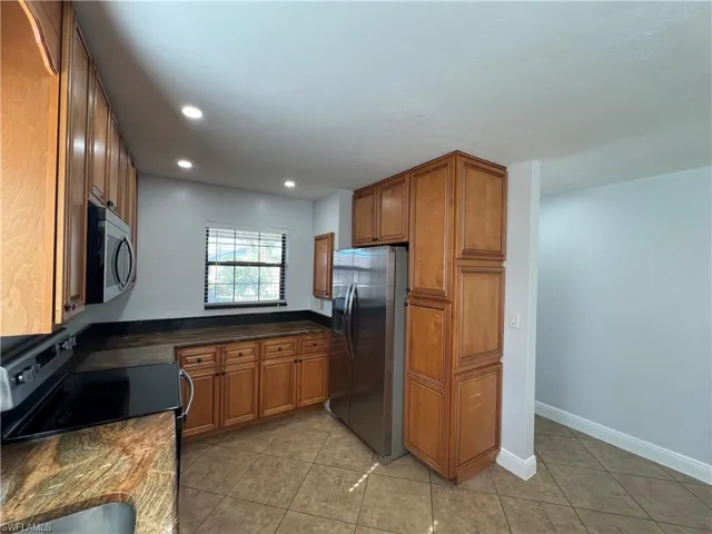Kitchen featuring wood finish cabinets, stainless steel appliances, light tile patterned floors, recessed lighting, and dark stone counters