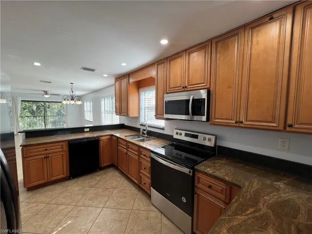 Kitchen featuring stainless steel appliances, wood finish cabinetry, hanging lights, dark stone countertops, and light tile patterned floors