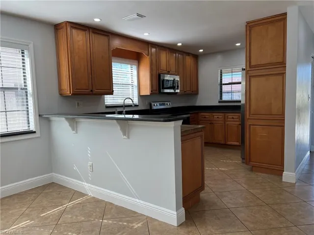 Kitchen featuring wood finish cabinets, a kitchen breakfast bar, a peninsula, light tile patterned floors, and stainless steel microwave